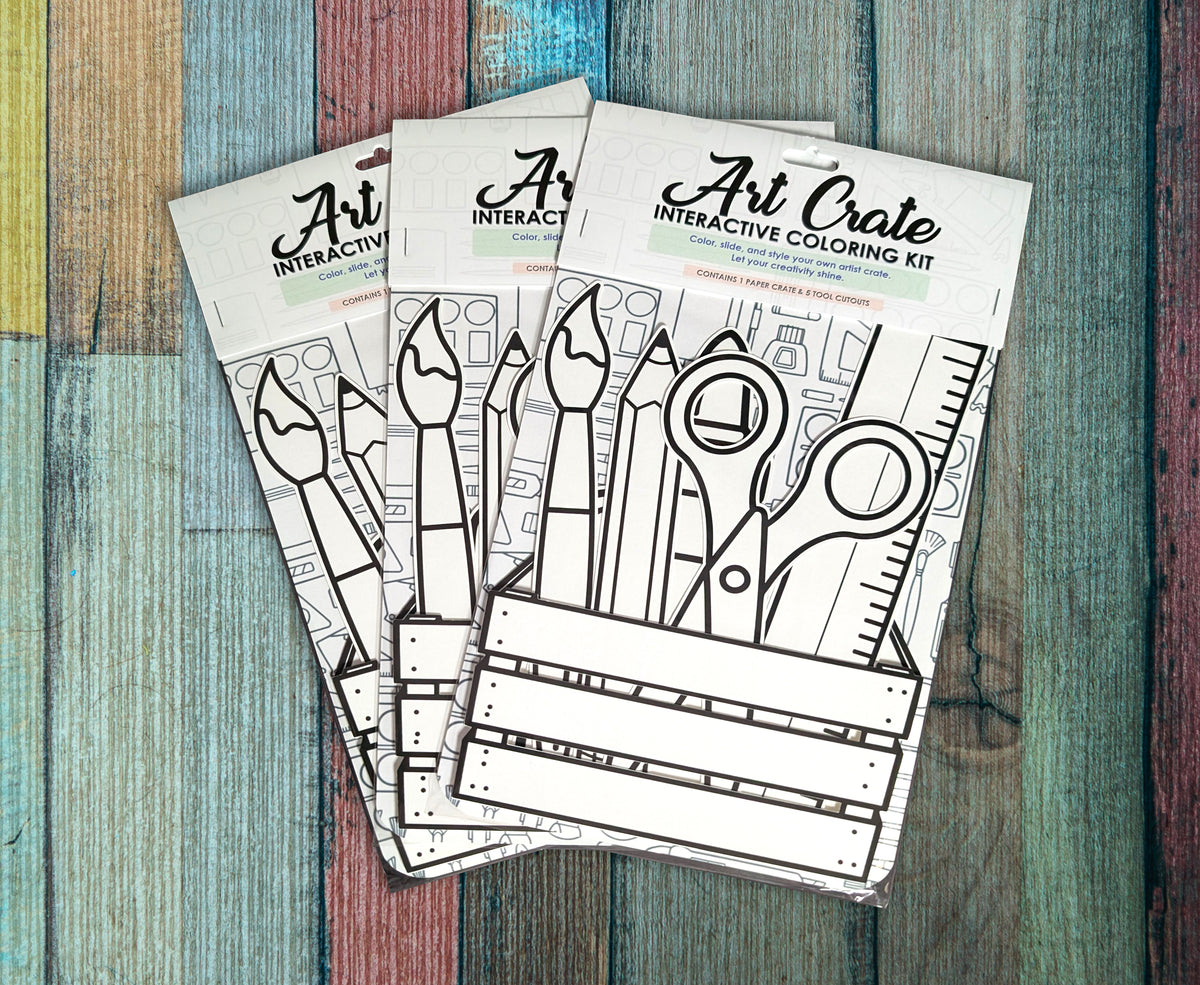 Three Art Crate interactive coloring kits arranged on painted wood, each in its packaging with the uncolored tool cutouts visible.