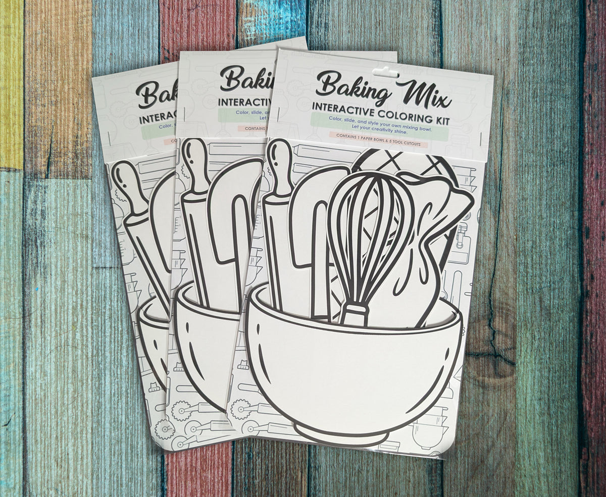 Three Baking Mix interactive coloring kits arranged on painted wood, each in its packaging with the uncolored bowl and utensil cutouts visible.