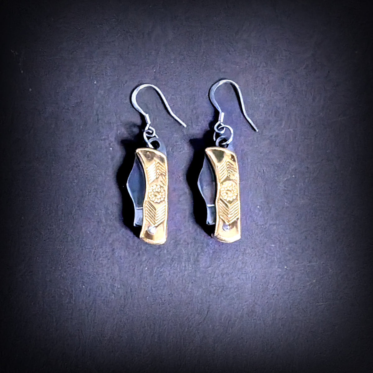 Brass flower mini pocket knife earrings by Pocket & Bear Collective, the pair hanging closed against a deep purple background, showing the engraved brass flower handles