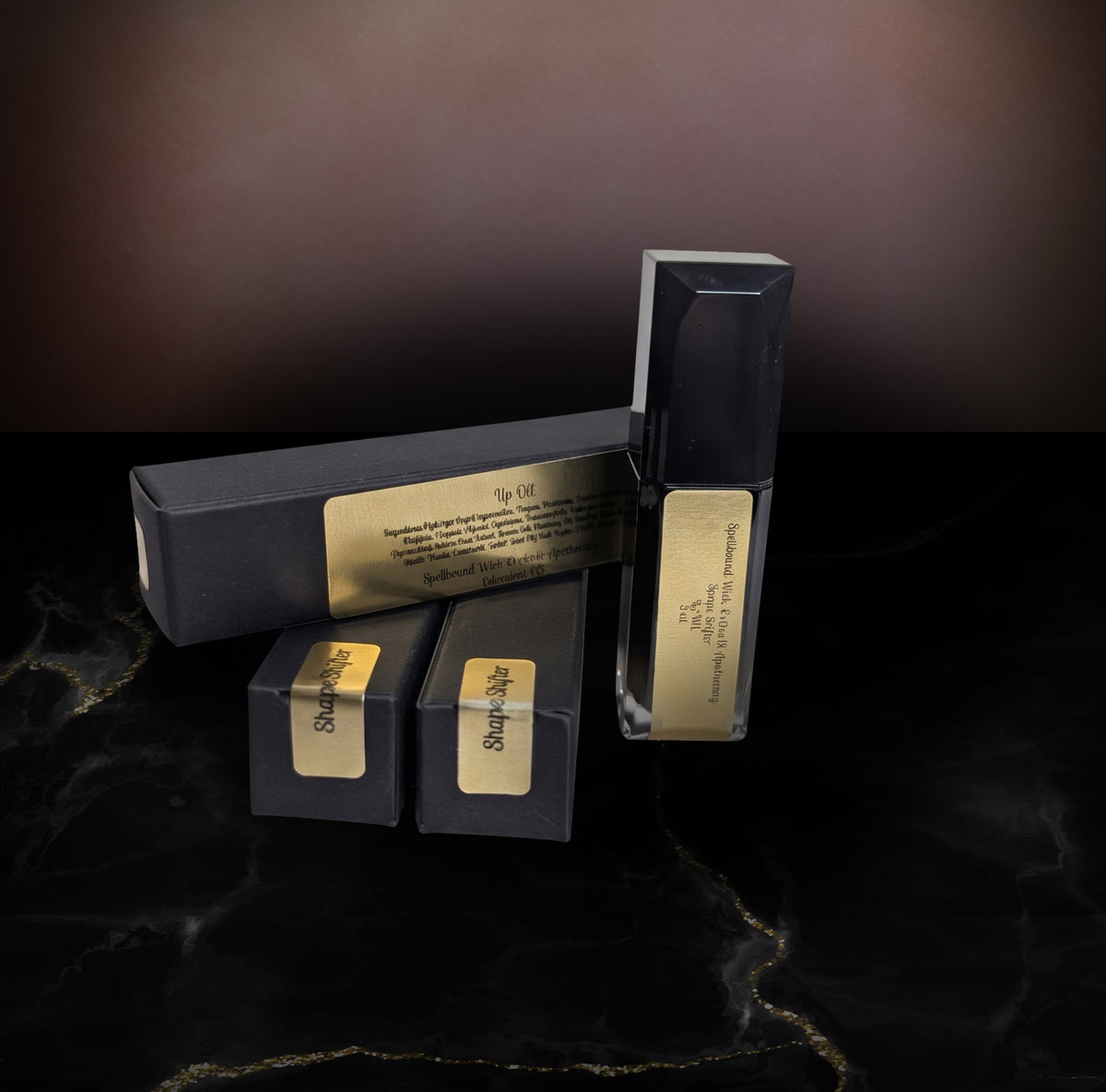 Black lip oil bottle and its black boxes arranged on dark marble, each box carrying a gold Spellbound Wick Works & Apothecary label.