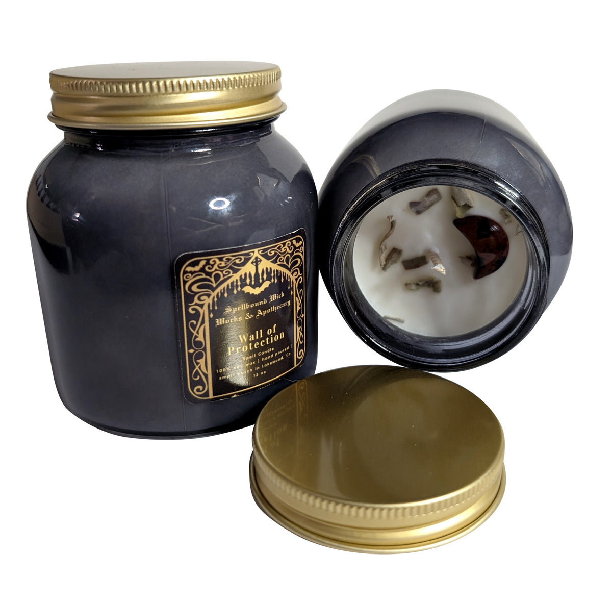 Two black jar candles on a marble surface, one open with its gold lid resting in front, the other closed with the gold label facing forward.