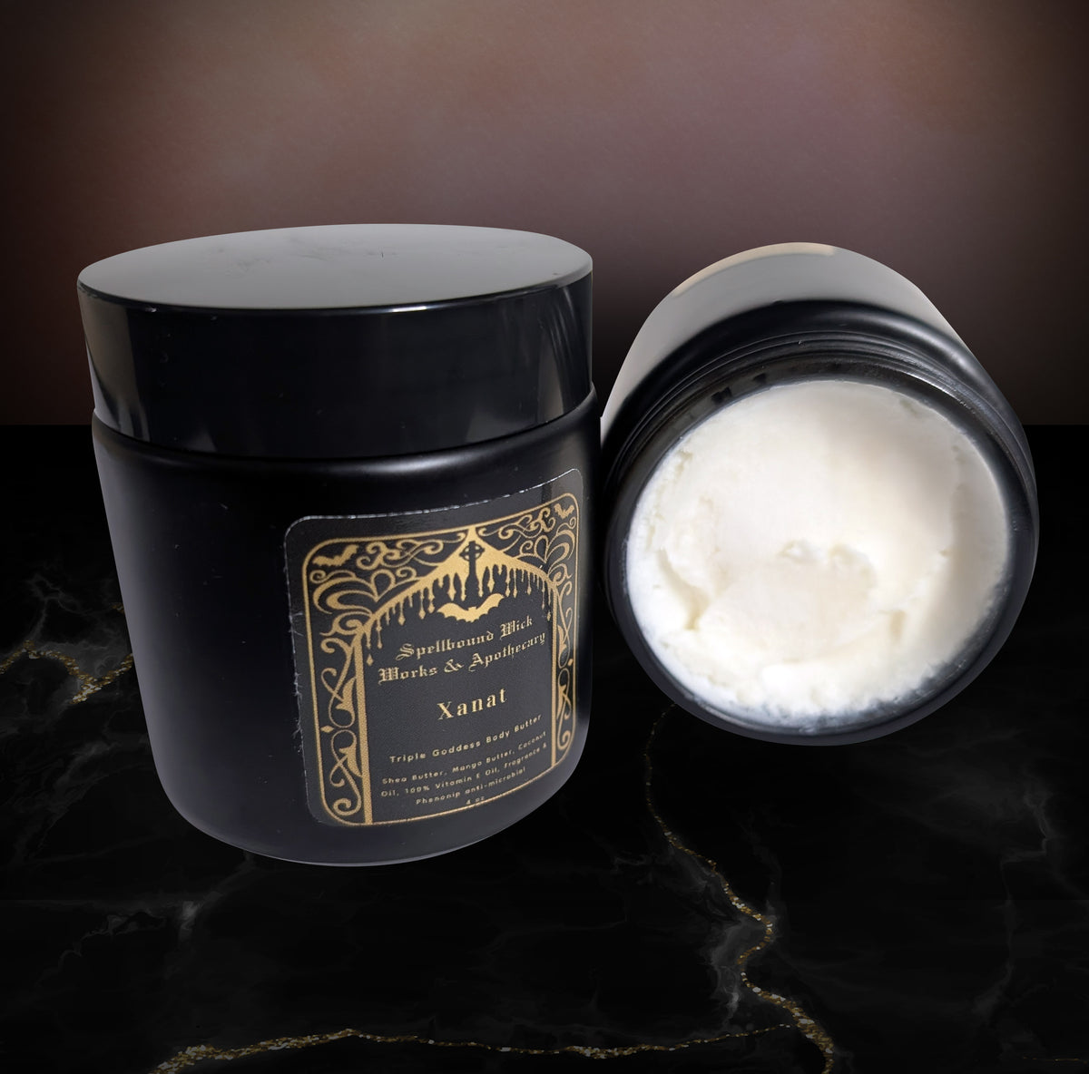Black jar of body butter with a black lid, shown open beside the closed jar, the whipped white butter smooth across the top, gold label reading Xanat.
