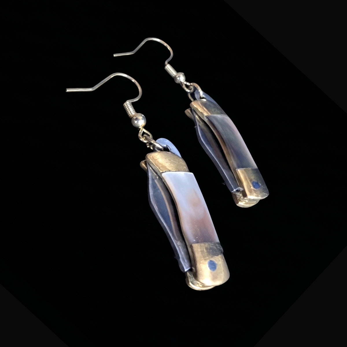 Dark shell mini pocket knife earrings by Pocket & Bear Collective closed, shown on their own against a black background with the gold plated earring hooks visible
