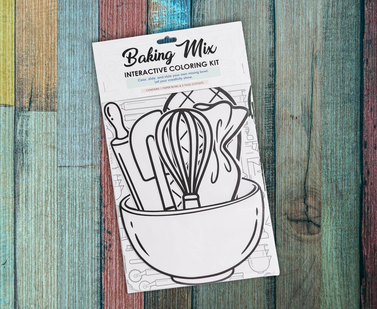 Single Baking Mix interactive coloring kit lying on a painted wood background, the uncolored mixing bowl, whisk and rolling pin cutouts showing through the front of the package below the Baking Mix header card.