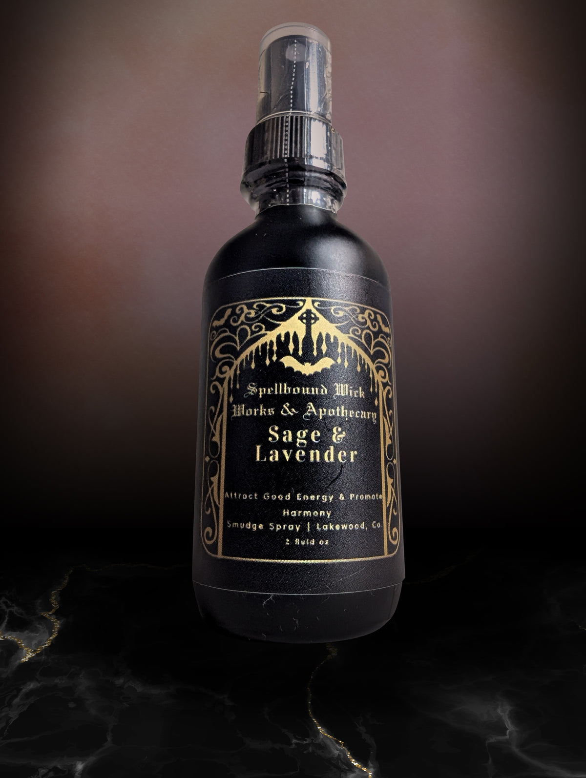 Single matte black spray bottle on dark marble, the gold arched label reading Sage & Lavender facing forward.
