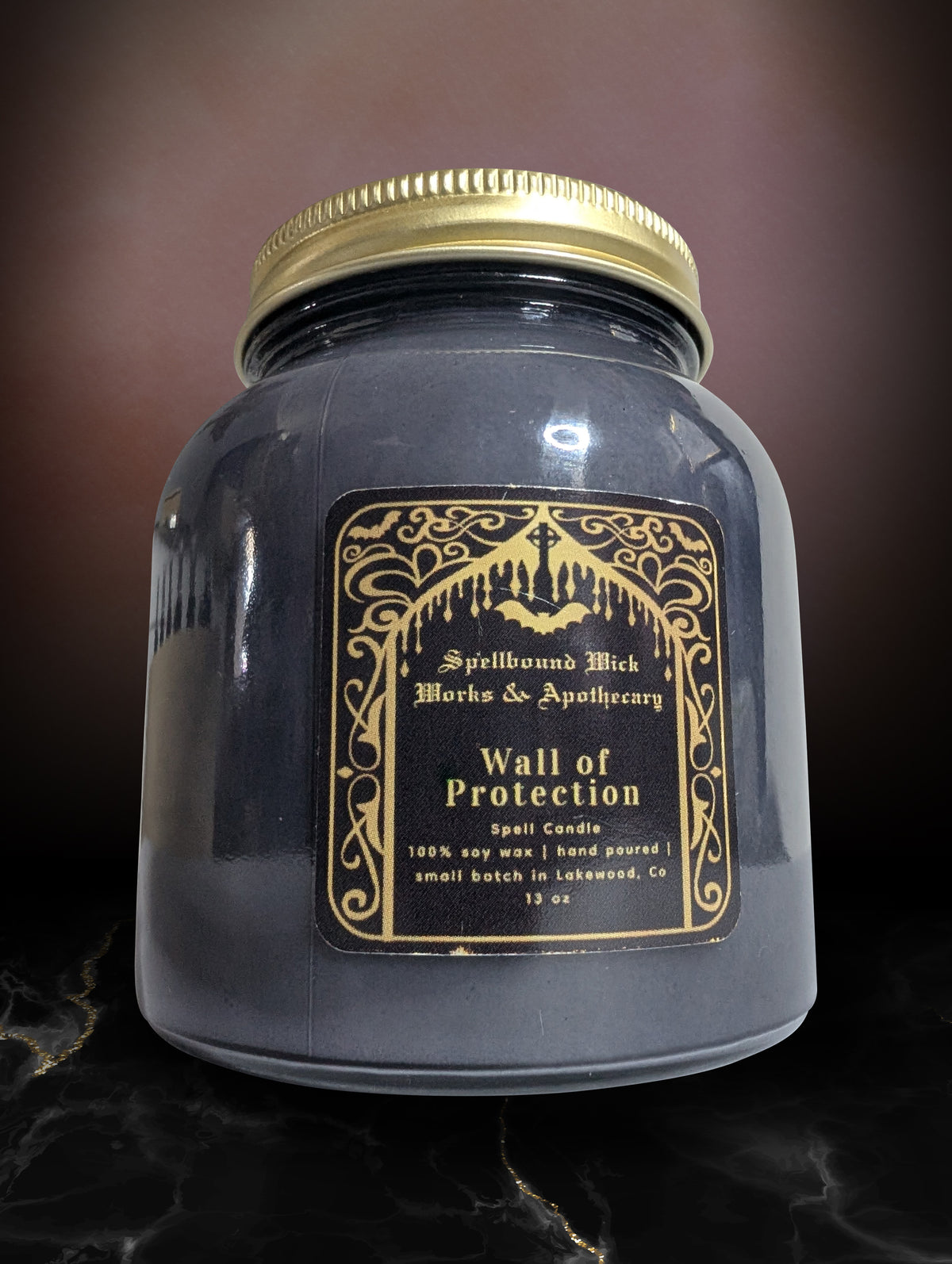 Black jar candle photographed at an angle on marble, gold lid and gold label catching the light.