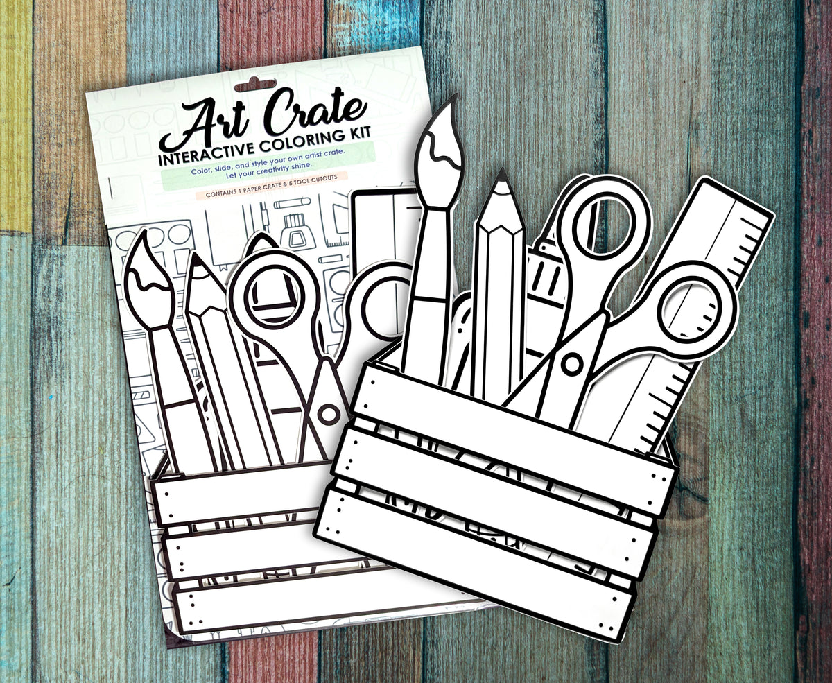 Two Art Crate interactive coloring kits in their packaging on a painted wood background, showing the uncolored paintbrush, pencil, scissors and ruler cutouts above the crate.