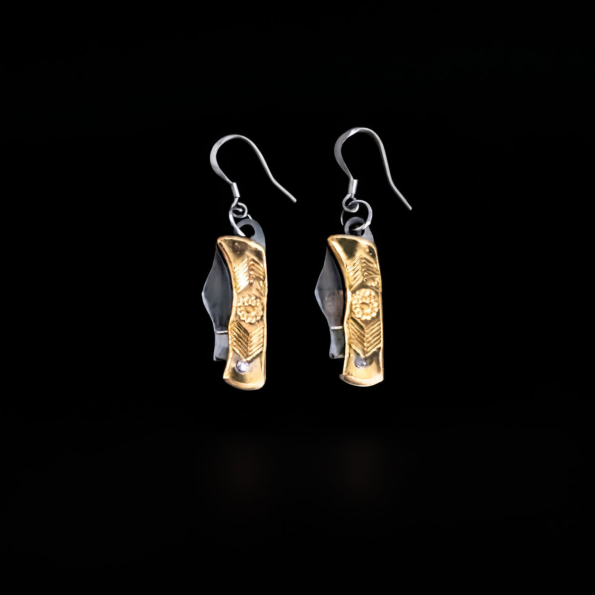 Brass flower mini pocket knife earrings by Pocket & Bear Collective, a pair of folded mini pocket knives with engraved brass flower handles and stainless steel earring hooks, on a black background