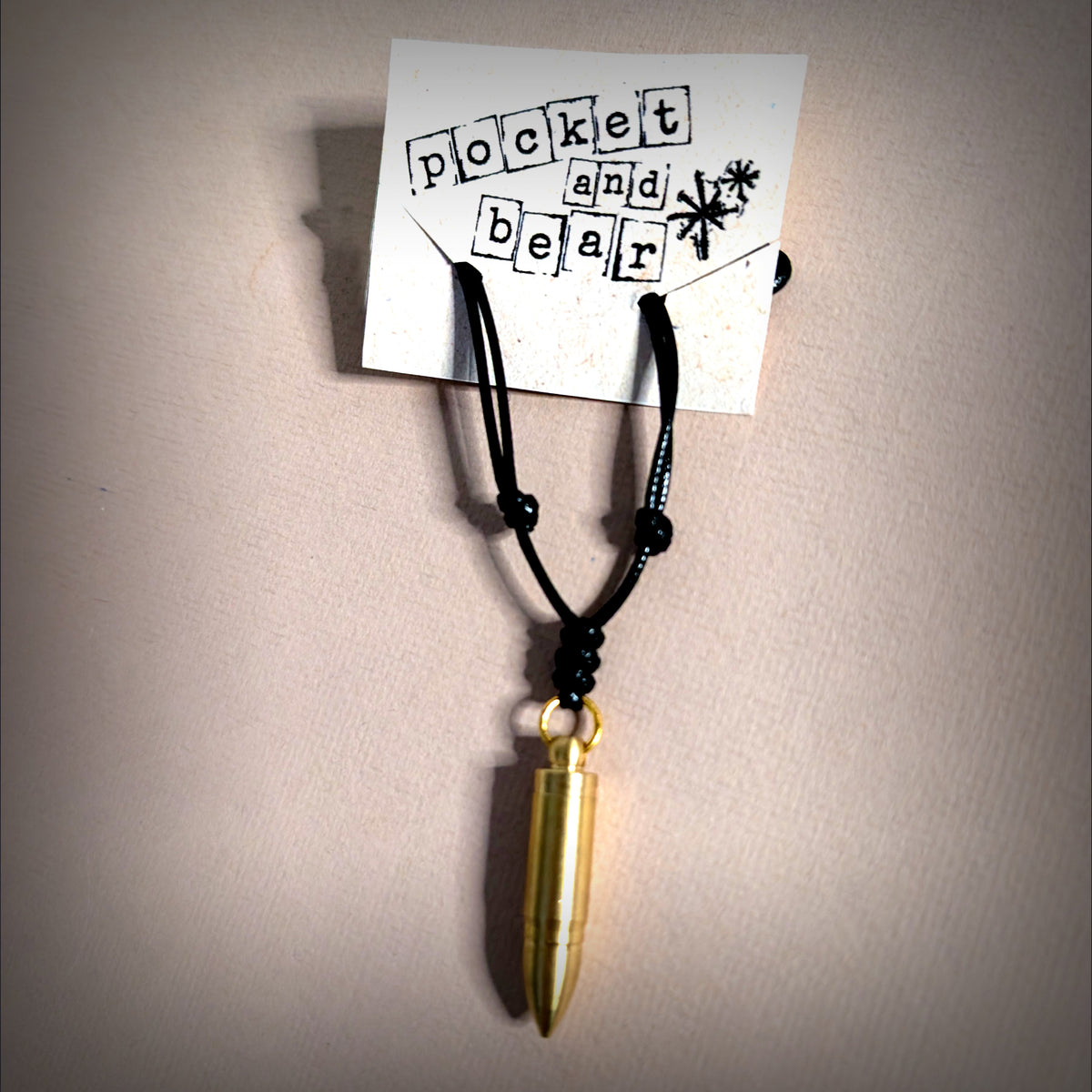 Bullet mini knife necklace by Pocket & Bear Collective laid flat on a cream background with a stamped Pocket and Bear card, the brass bullet pendant closed