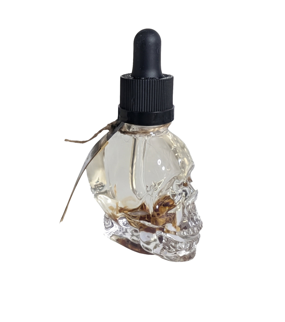 Side view of the clear skull shaped bottle on a white background, black dropper top in place and botanicals suspended in the oil.