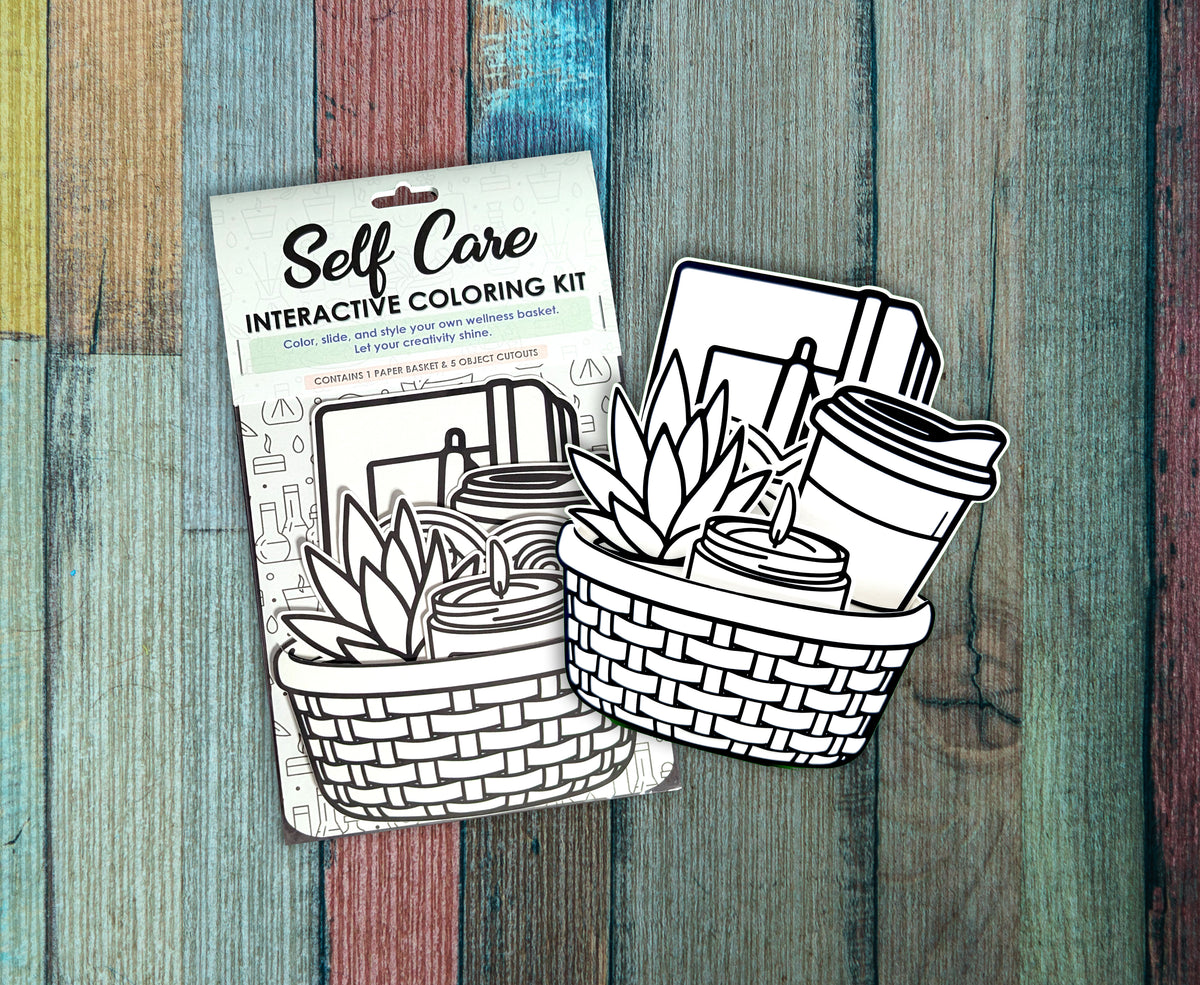 Two Self Care interactive coloring kits in their packaging on a painted wood background, showing the uncolored basket and self care cutouts behind the Self Care header card.