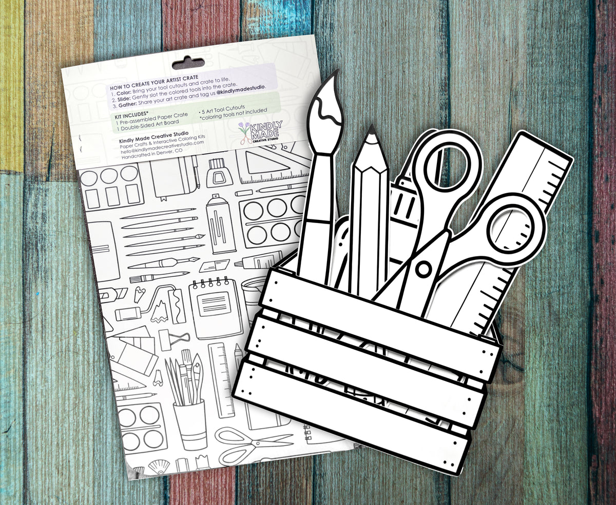Back of the Art Crate kit on painted wood, showing the how to instructions and the double sided art board covered in art supply line drawings, with the assembled crate and cutouts in front.