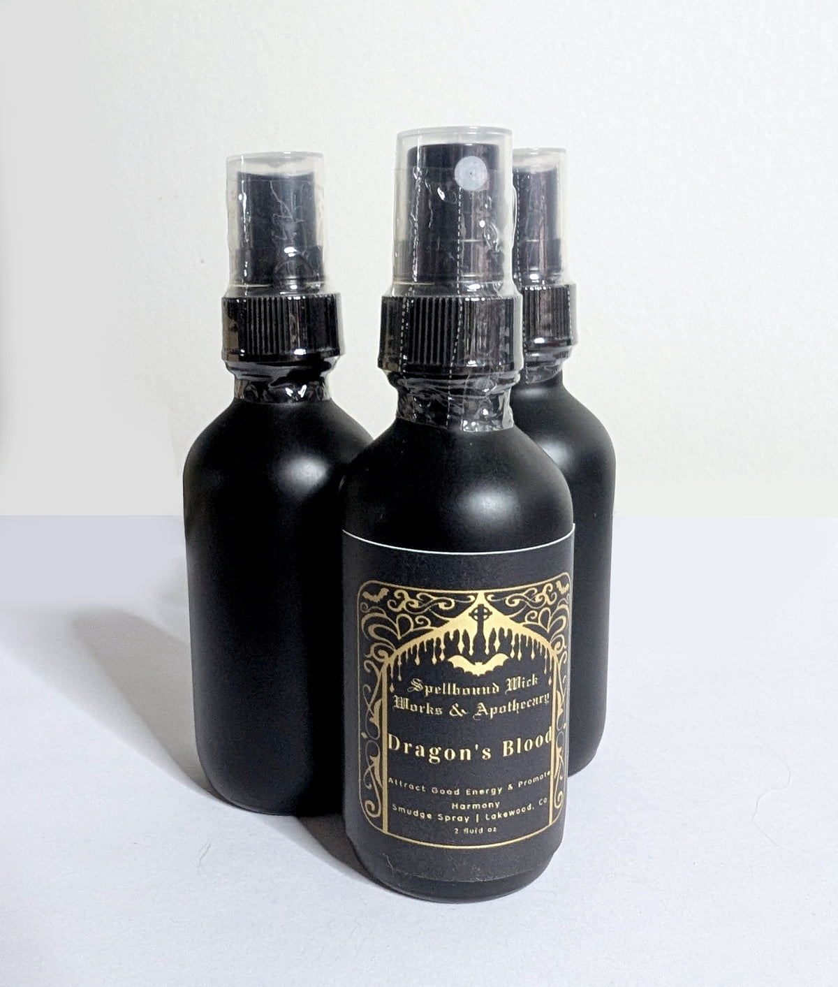 Three matte black spray bottles clustered at an angle on a white background, labels facing the camera.