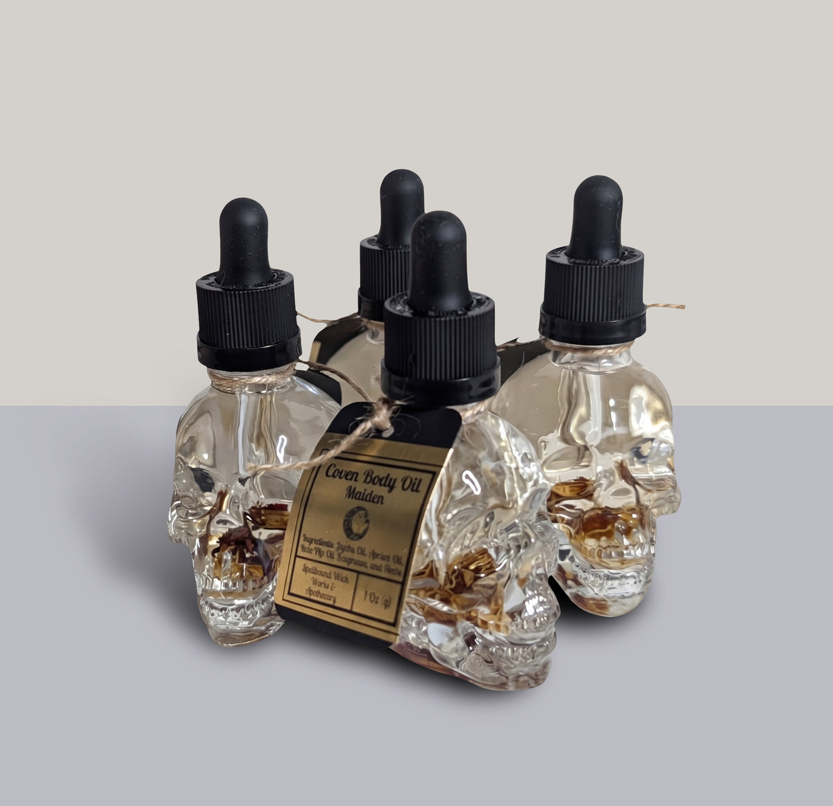 Clear skull shaped glass dropper bottles of Coven Body Oil Maiden photographed together against a pale background.