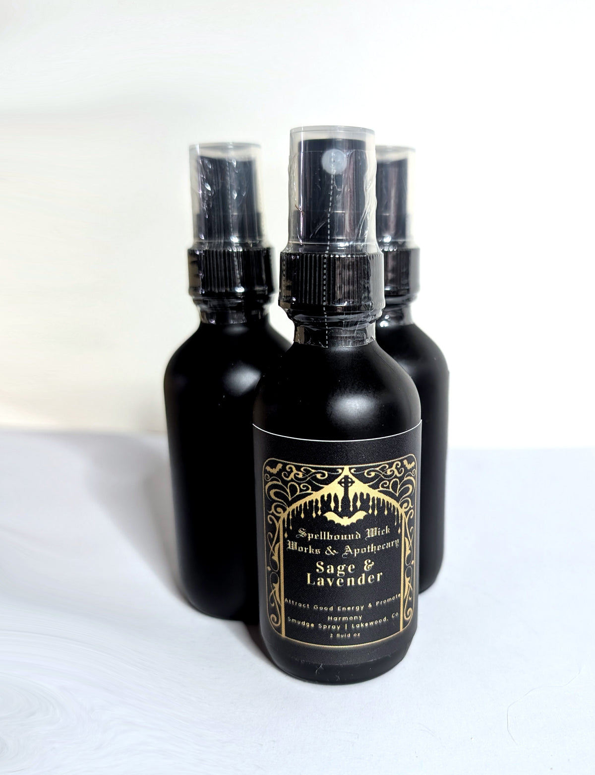 Matte black spray bottles photographed together against a pale background, gold labels facing the camera.