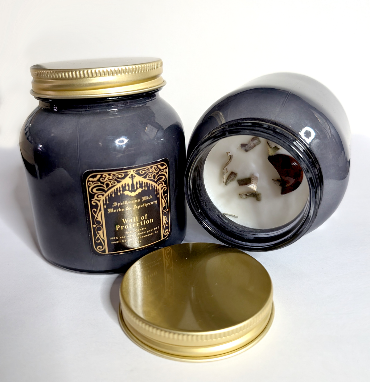 Open black jar candle showing the poured soy wax and hemp wick, gold lid lying flat beside it, second closed jar behind.
