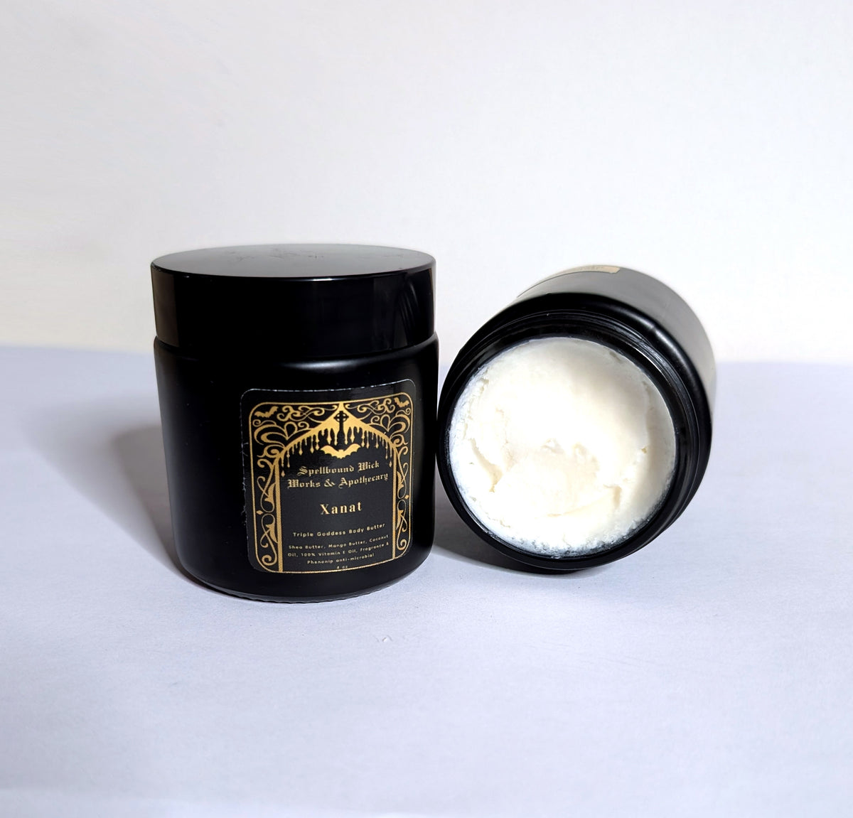 Open black jar showing the whipped white body butter, lid set behind it on a white background.