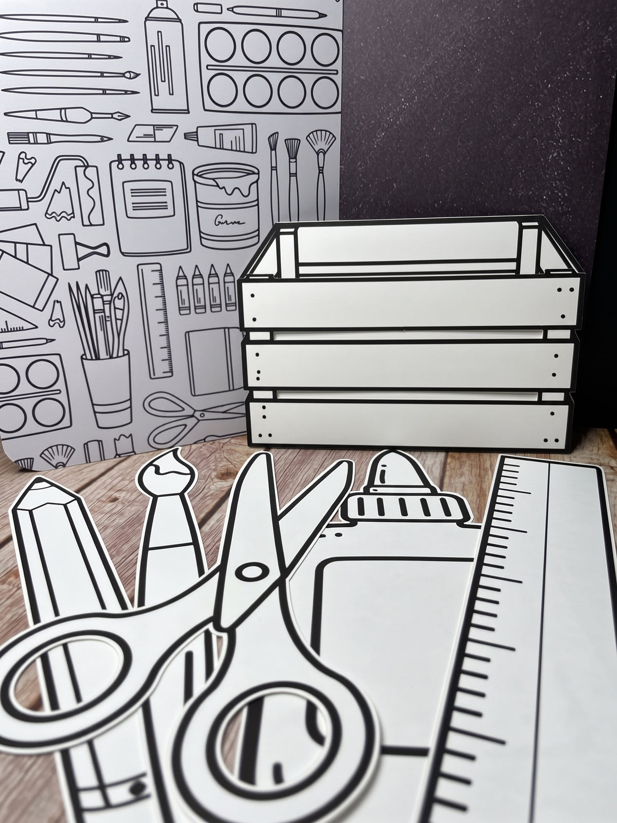 The five Art Crate cutouts laid out on wood, the crate standing in front of the art board with a pencil, paintbrush, scissors, paint tube and ruler arranged below it.
