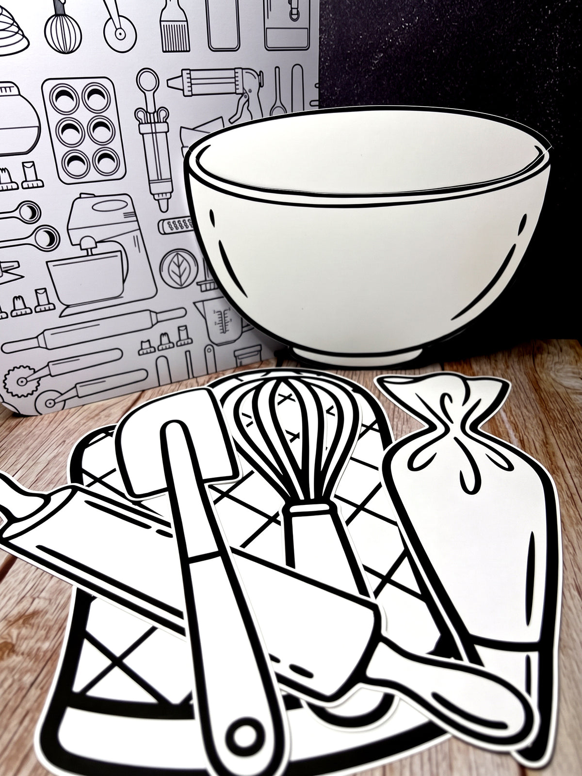 The five Baking Mix cutouts laid out on wood, the mixing bowl standing in front of the art board with the whisk, spatula, rolling pin and piping bag arranged below it.