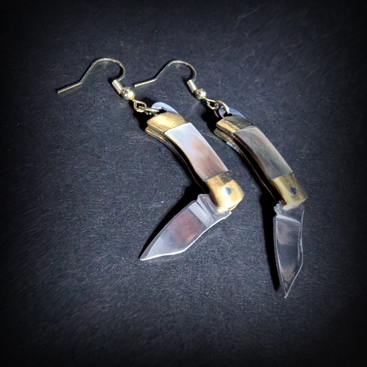 Dark shell mini pocket knife earrings by Pocket & Bear Collective with both stainless steel blades swung open on a grey background