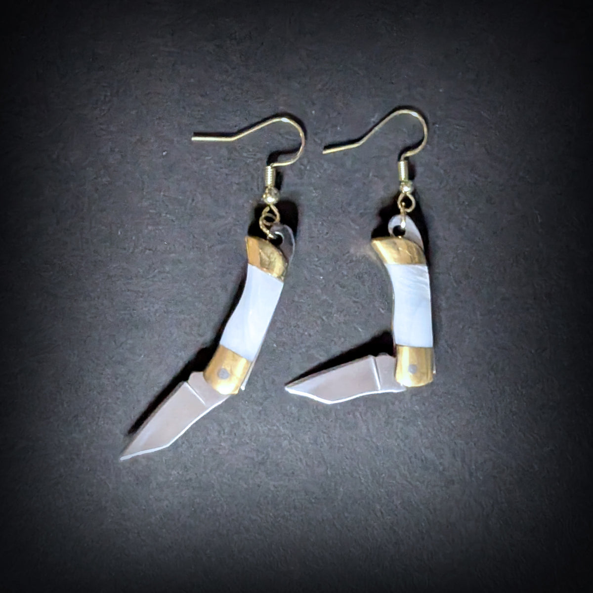 White shell mini pocket knife earrings by Pocket & Bear Collective with both stainless steel blades swung open on a grey background
