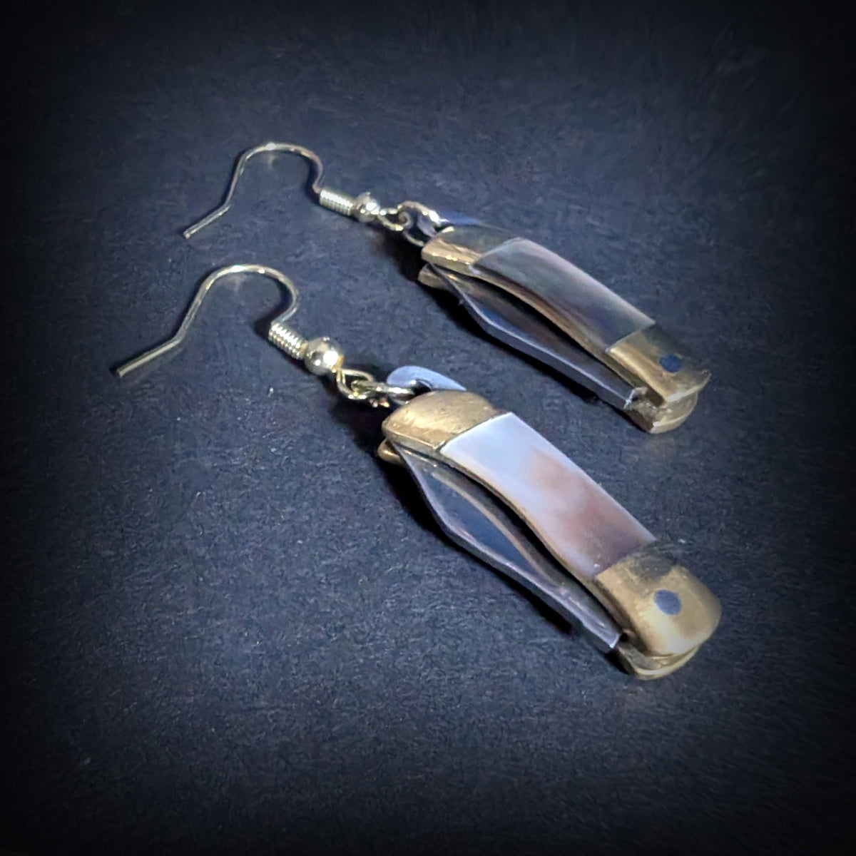 Dark shell mini pocket knife earrings by Pocket & Bear Collective closed, shown close up on grey with the natural dark shell handle and brass bolsters filling the frame