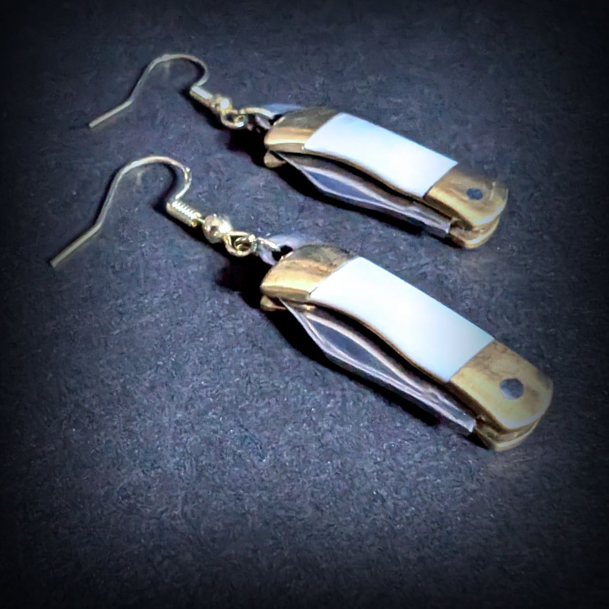 White shell mini pocket knife earrings by Pocket & Bear Collective closed, shown close up on grey, with the natural white shell handle and brass bolsters in full view