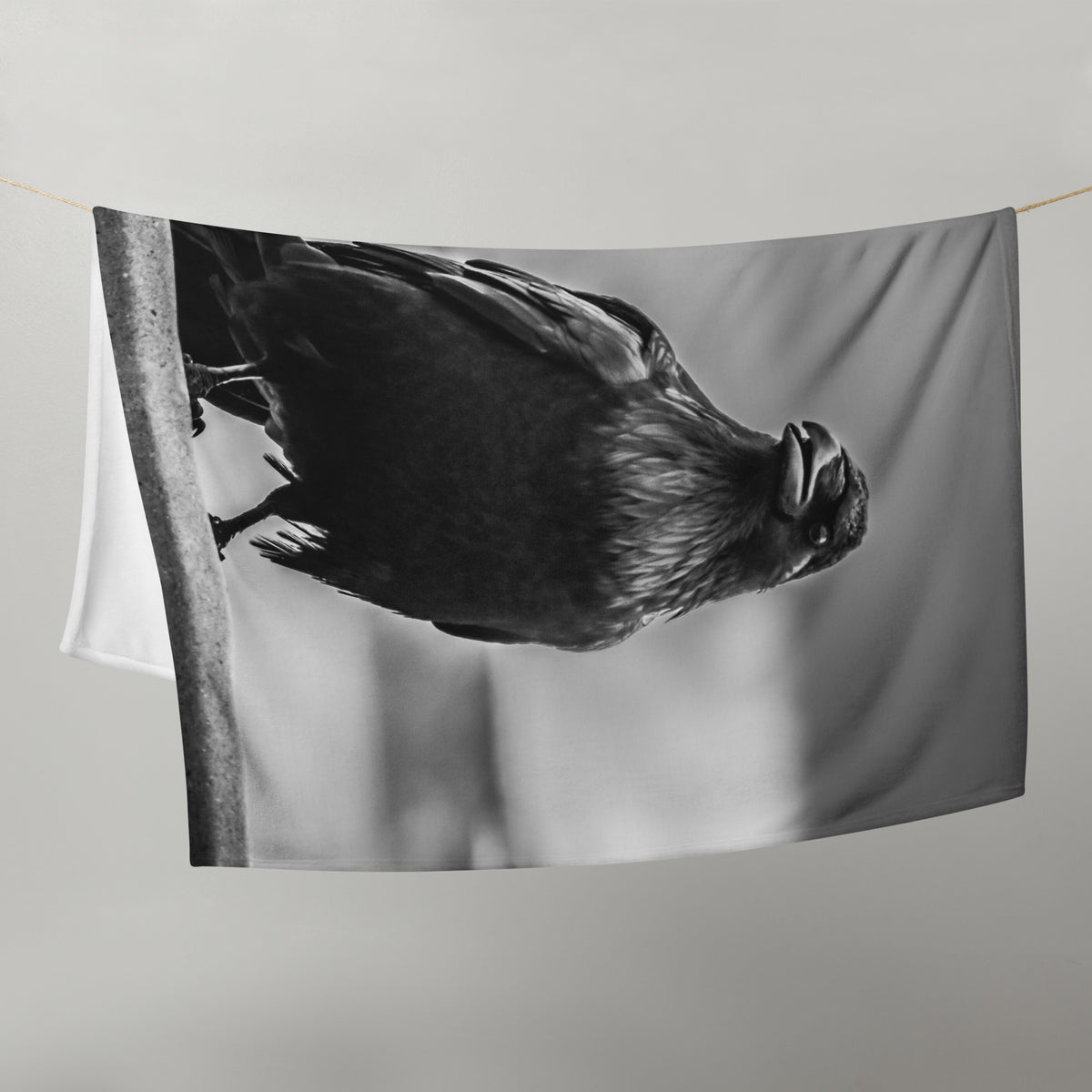 Crow So Chic throw blanket by Iain Camacho, draped and hanging to show the black and white crow photograph printed on the front