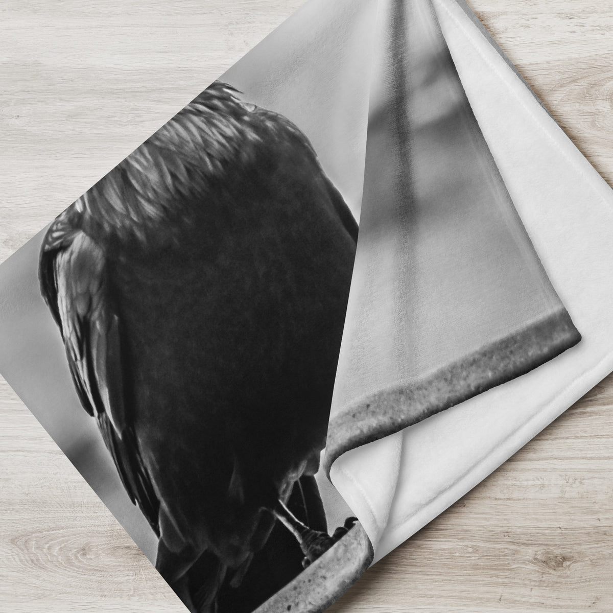 Crow So Chic throw blanket by Iain Camacho, corner folded back to show the black and white crow photograph on the front and the white reverse side