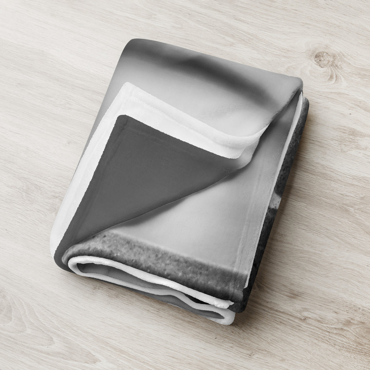Crow So Chic throw blanket by Iain Camacho, folded on a light wood floor showing the black and white print and white reverse side