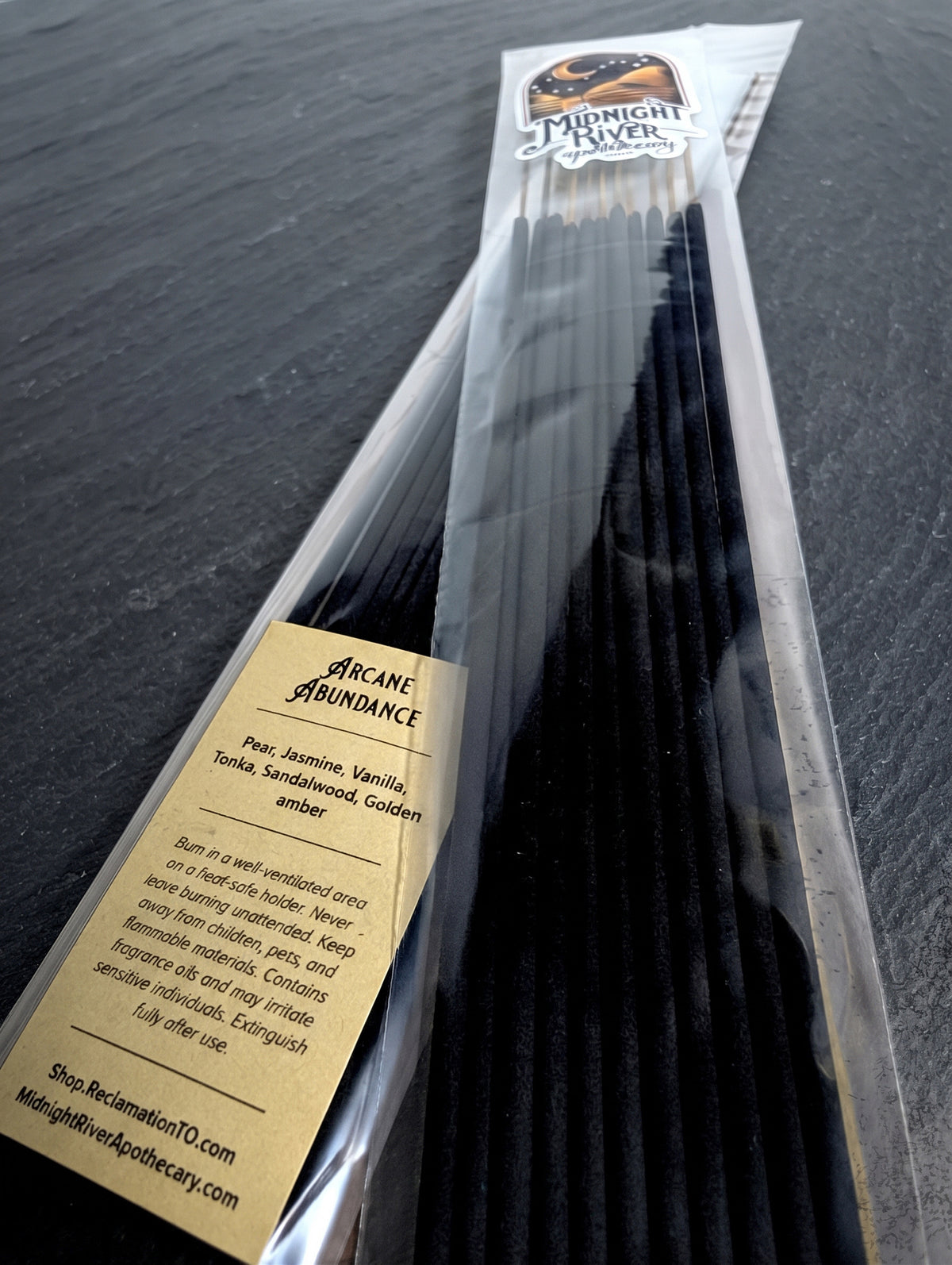 Angled close view of the incense bundle in its clear bag on dark slate, with the cream-colored ingredient label visible at the lower left