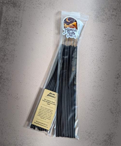 Overhead view of the clear bag of black incense sticks with the Midnight River Apothecary label, resting on a gray textured surface