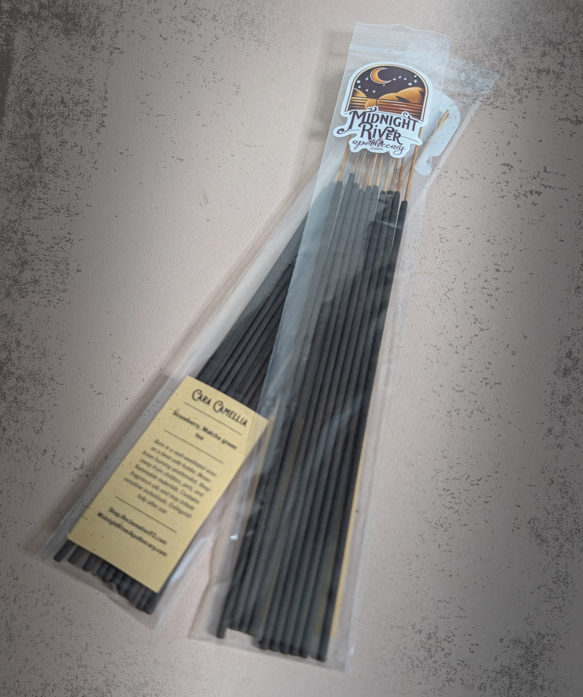 Angled view of the bagged black incense sticks on dark slate, with the cream ingredient label at the lower left