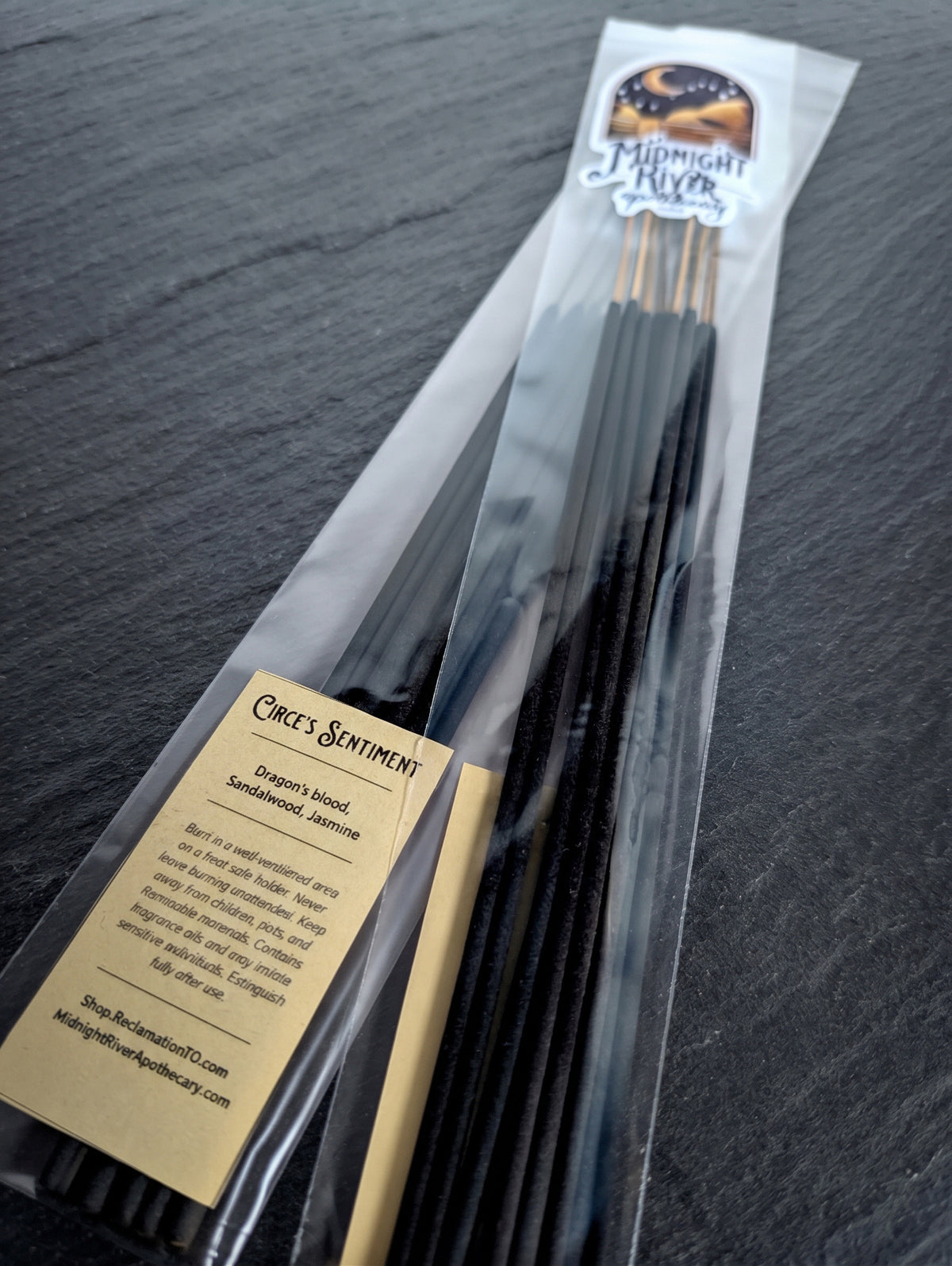 Pack of Circe’s Sentiment hand dipped incense by Midnight River Apothecary lying at an angle on dark slate, with the cream label reading “Circe’s Sentiment” on the clear bag and black sticks inside