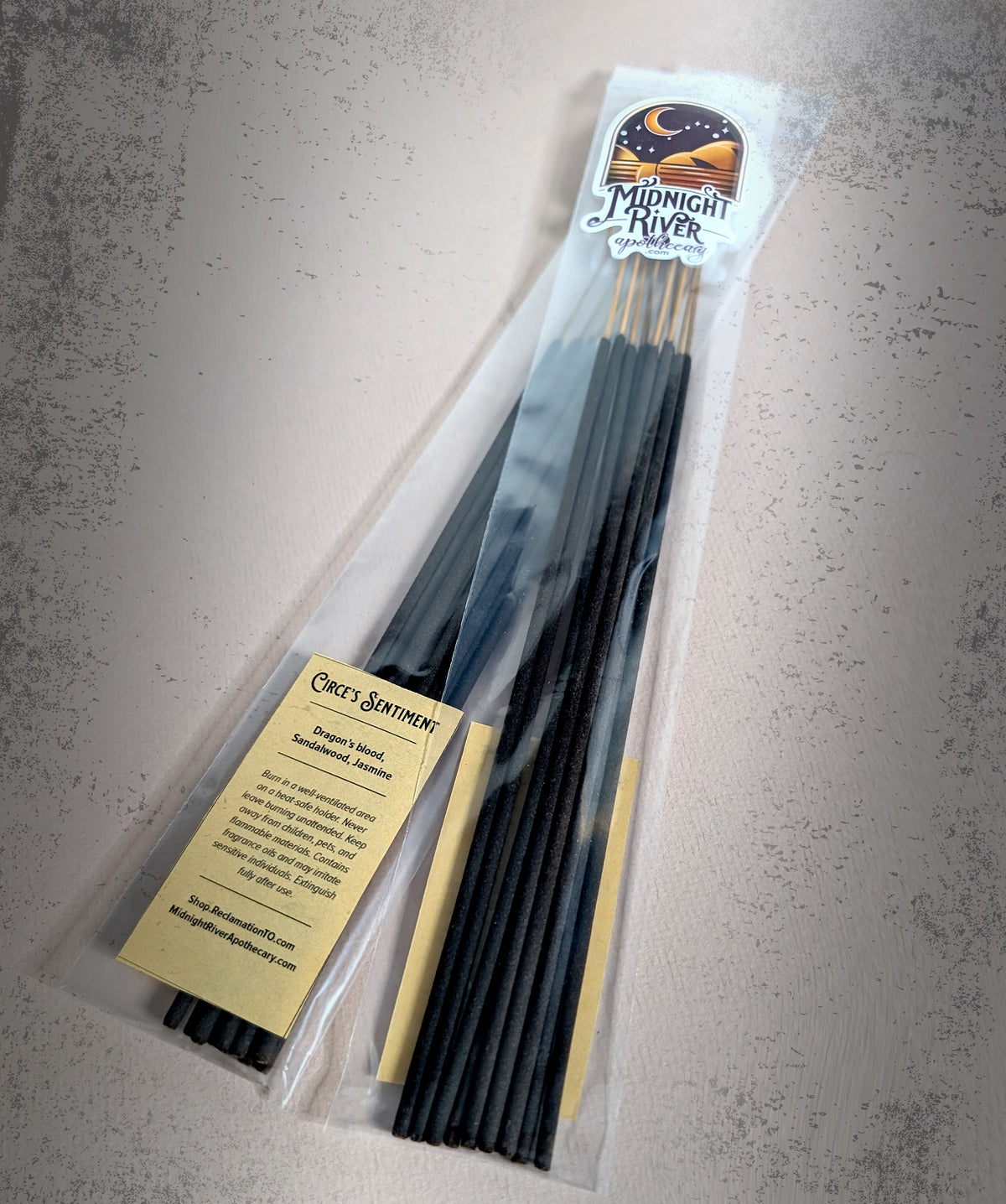 Bagged bundle of black incense sticks on a pale gray surface, with the cream label visible at the lower left