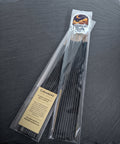 Clear bag of black hand dipped incense sticks with a Midnight River Apothecary Claircognizance label, lying on a dark slate surface.