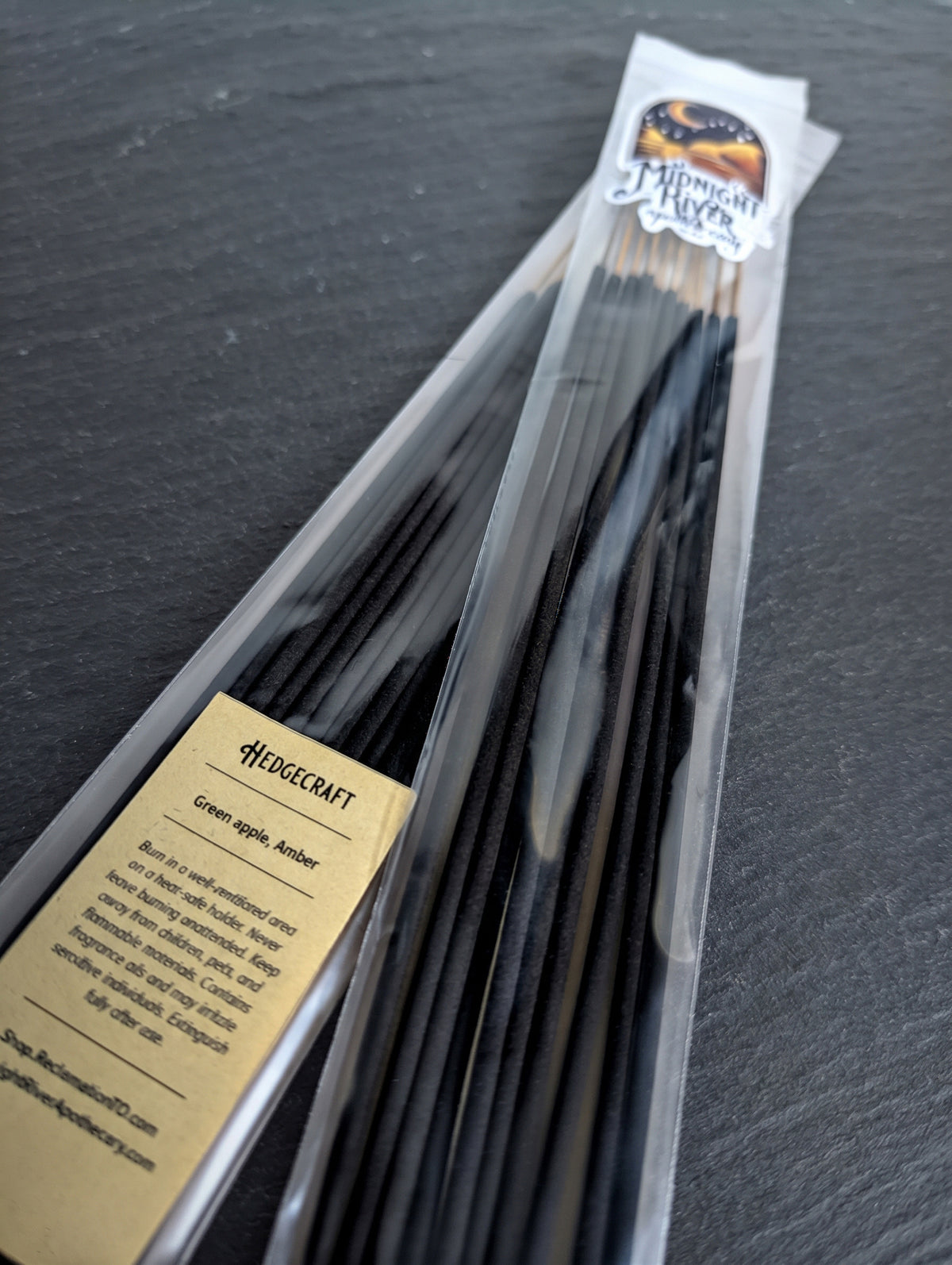 Angled view of the bagged incense bundle on a light surface, showing the label and the black sticks