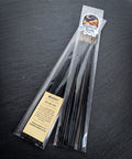 Pack of Hedgecraft hand dipped incense by Midnight River Apothecary lying at an angle on a dark slate surface, with a cream-colored ingredient label on the clear bag and black sticks inside