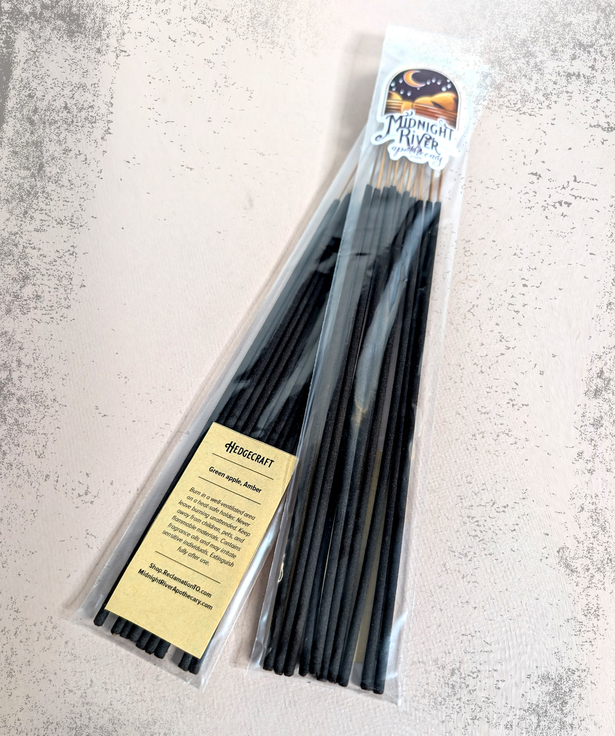 Overhead view of the clear bag of black incense sticks on a pale marbled surface, with the cream label at the lower left