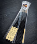 Clear bag of black hand dipped incense sticks with a Midnight River Apothecary Lyrical Lilith label, lying on a dark slate surface.