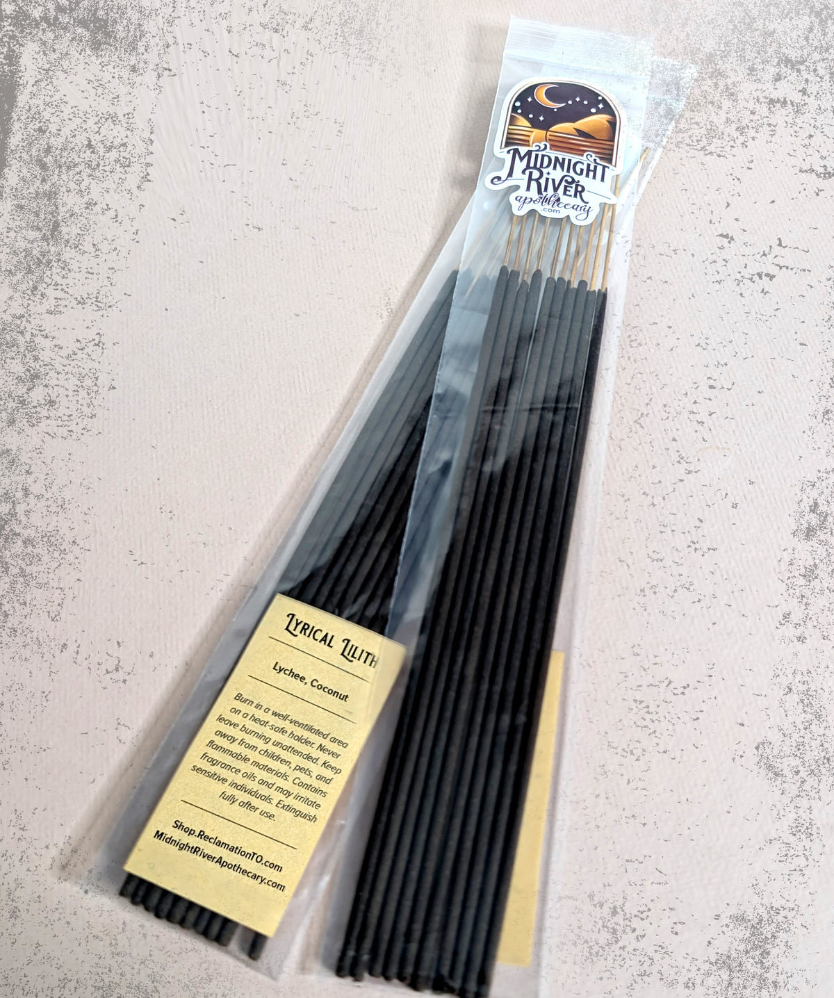 Bag of Lyrical Lilith hand dipped incense by Midnight River Apothecary on a light gray textured surface, with the yellow label showing the scent contents.