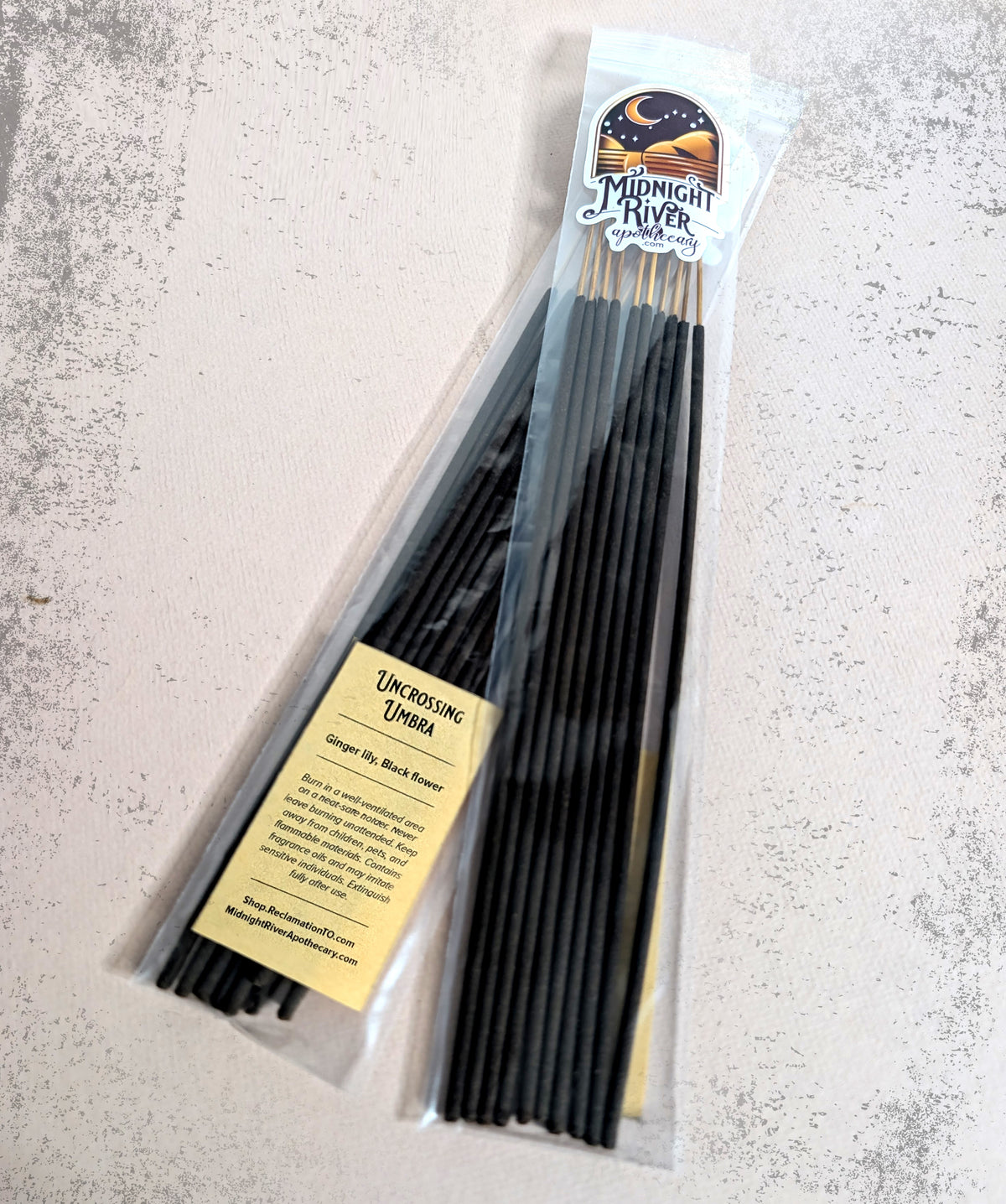 Bag of Uncrossing Umbra hand dipped incense by Midnight River Apothecary on a light gray textured surface, with the yellow label showing the scent contents.