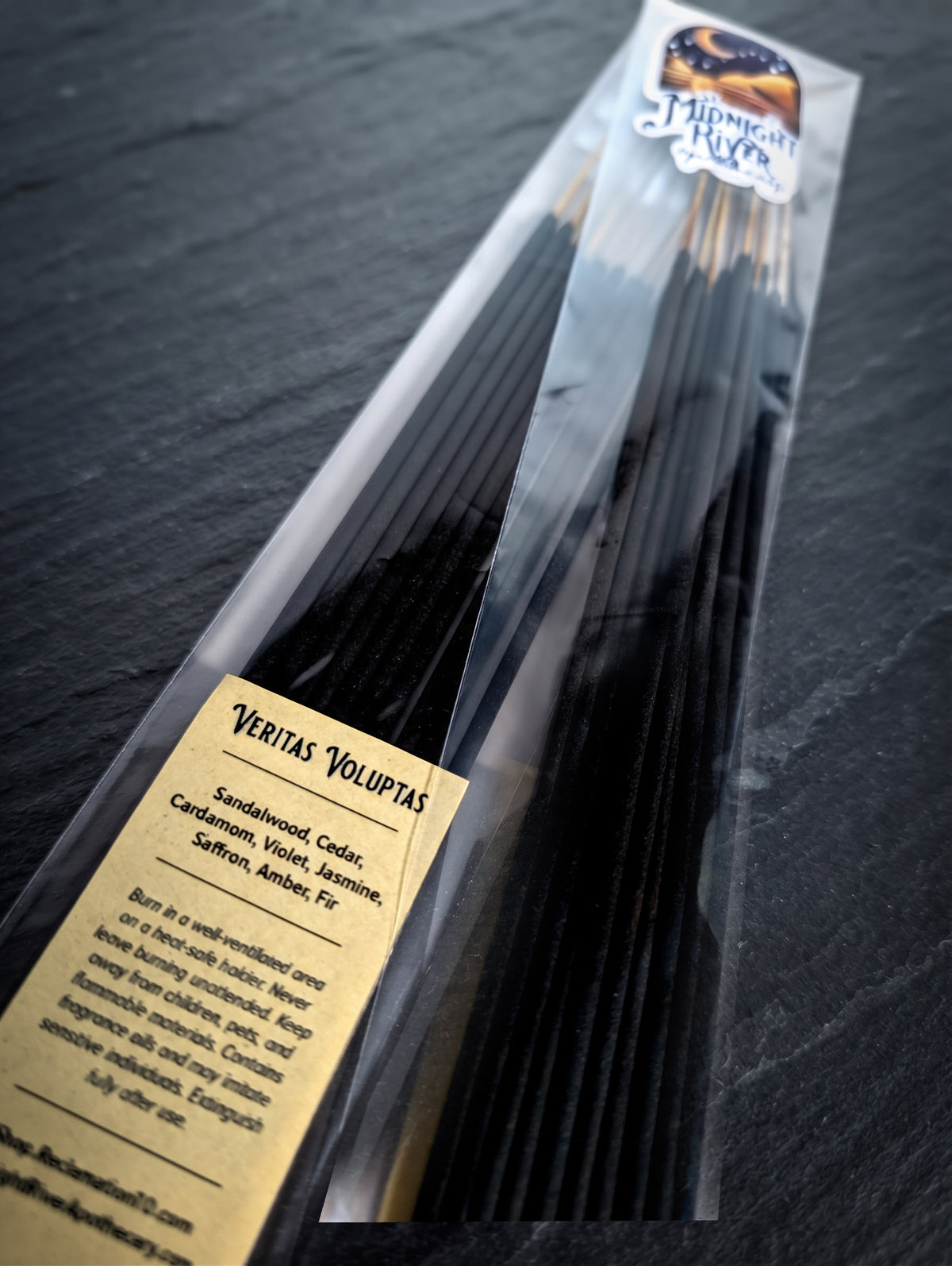 Angled view of the bagged black incense sticks on dark slate, showing the label and the tops of the sticks