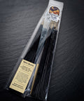 Pack of Veritas Voluptas hand dipped incense by Midnight River Apothecary lying at an angle on dark slate, with the cream label reading “Veritas Voluptas” on the clear bag and black sticks inside