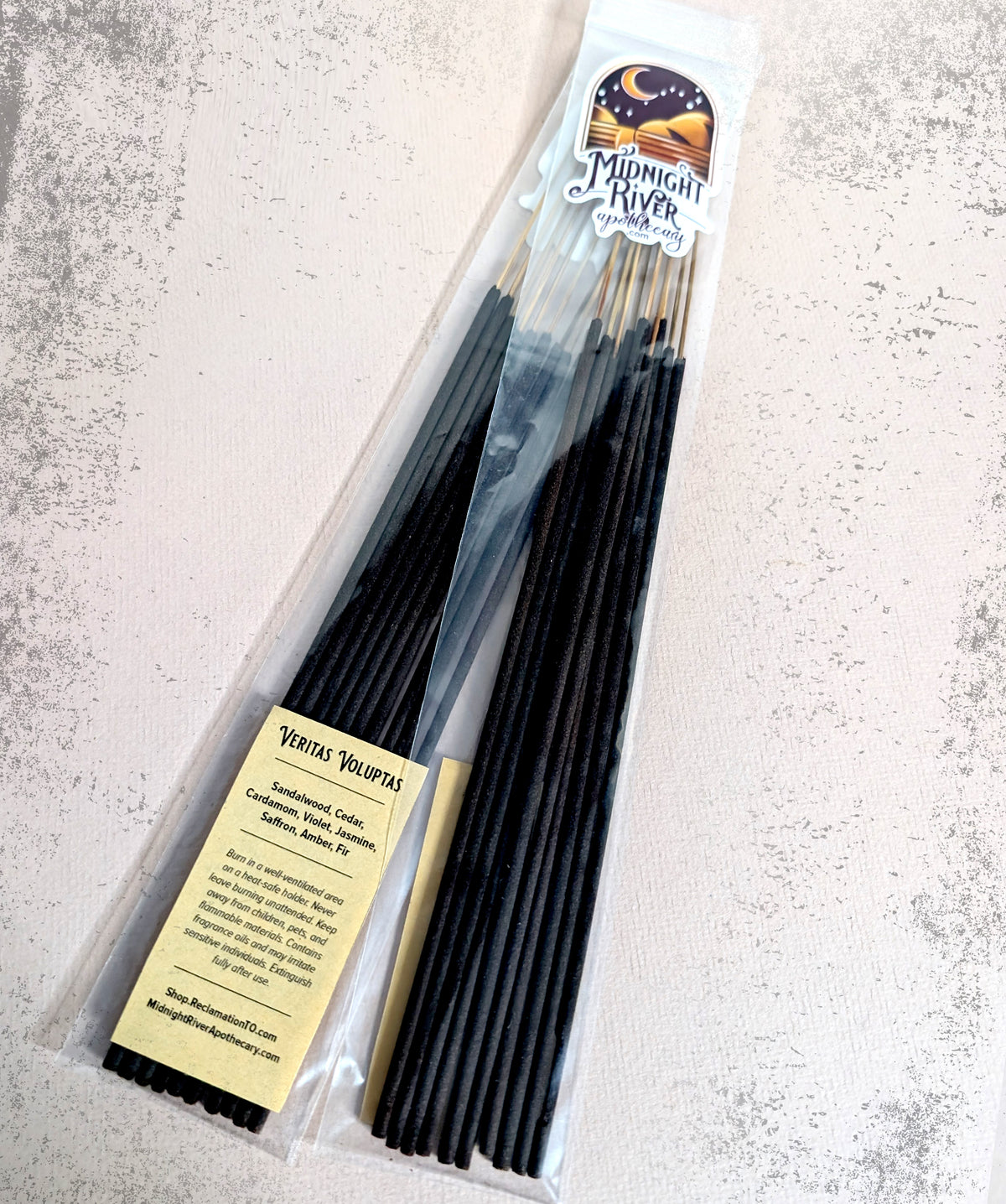 Bagged bundle of black incense sticks on a pale marbled surface, with the cream label at the lower left