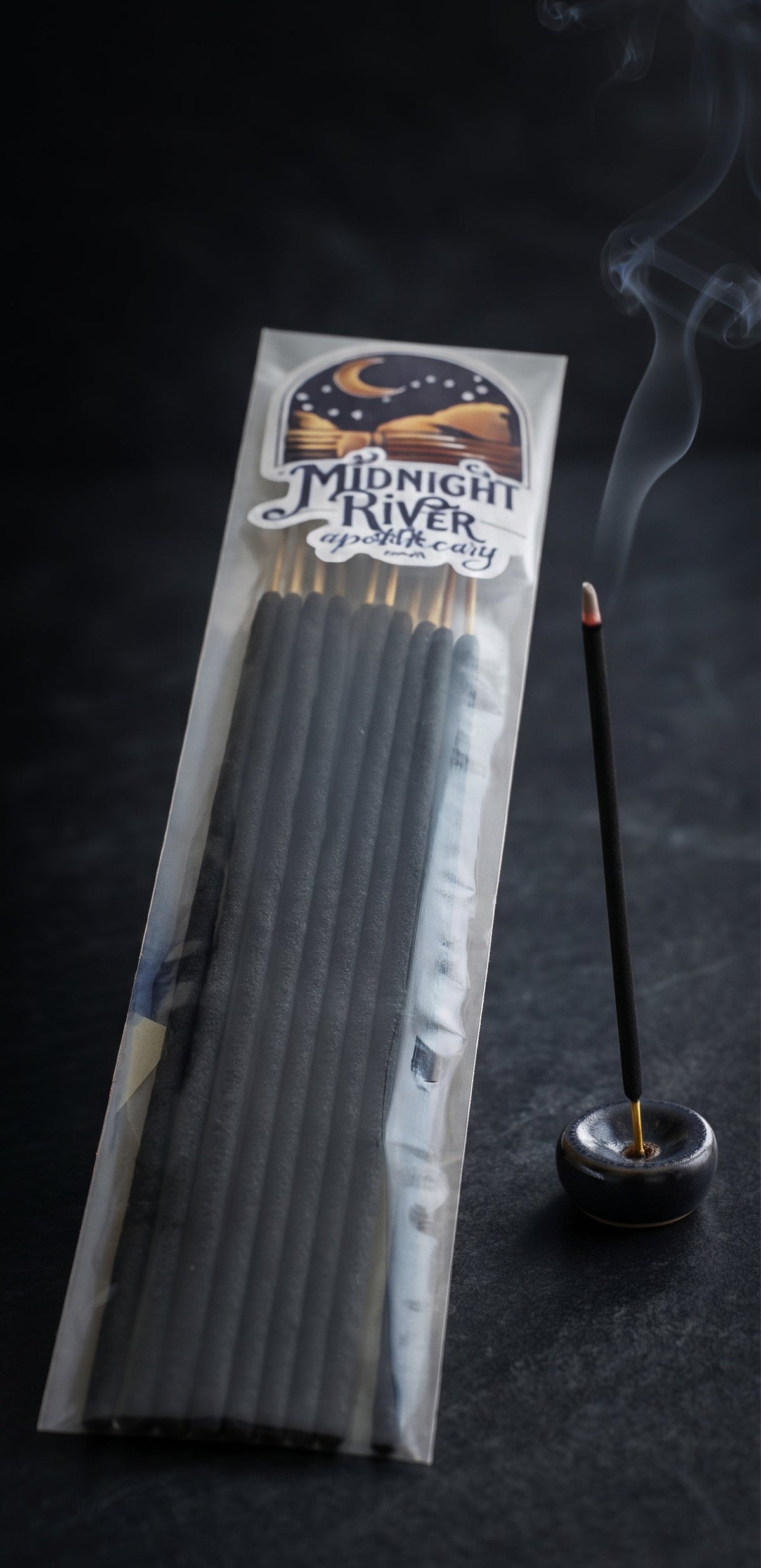 Tall view of the Lyrical Lilith incense bag standing beside a small black incense holder on a dark background.