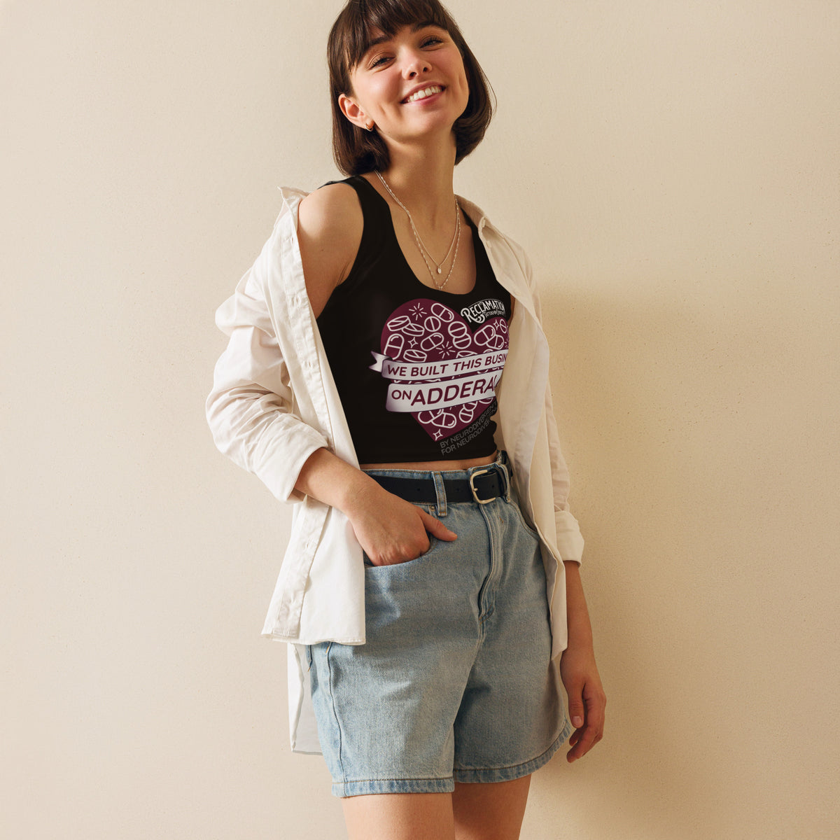 We Built This Business On Adderall crop top worn by a model with an open jacket and denim shorts, the dark red pill-filled heart and banner print across the front