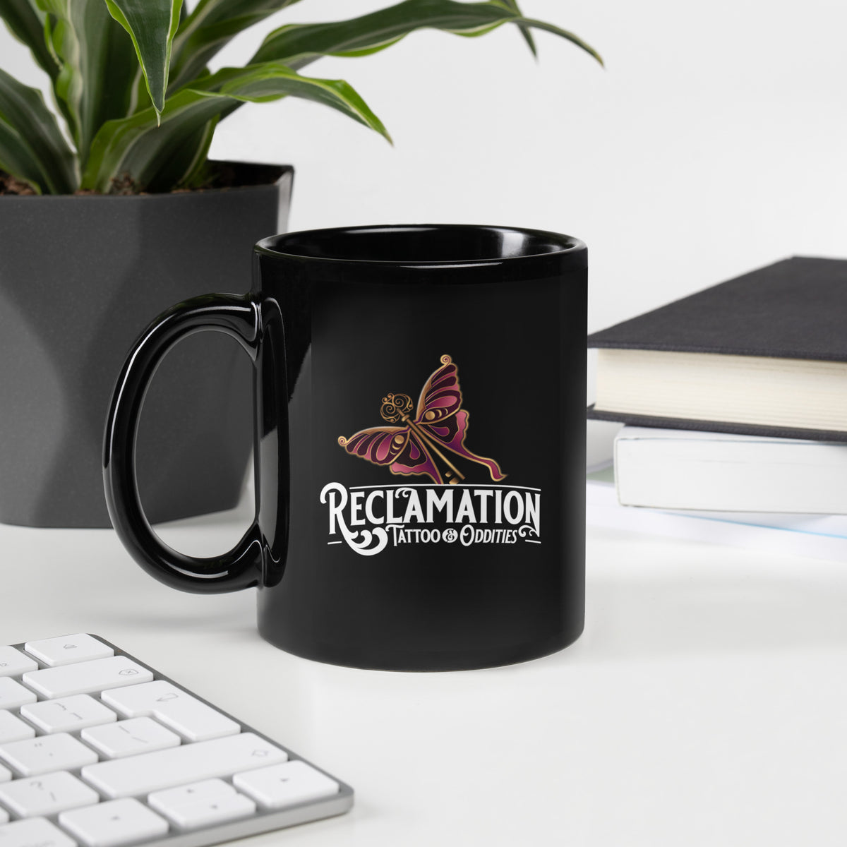 Reclamation & Midnight River mug, handle on the left, close view of the Reclamation Tattoo & Oddities butterfly and key logo on the black glossy ceramic