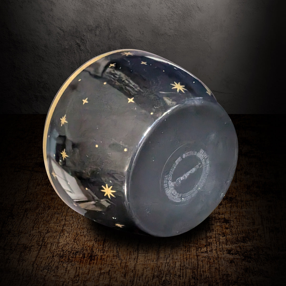 Black star candle tipped onto its rim on a dark background, showing the gold stars painted across the underside of the bowl