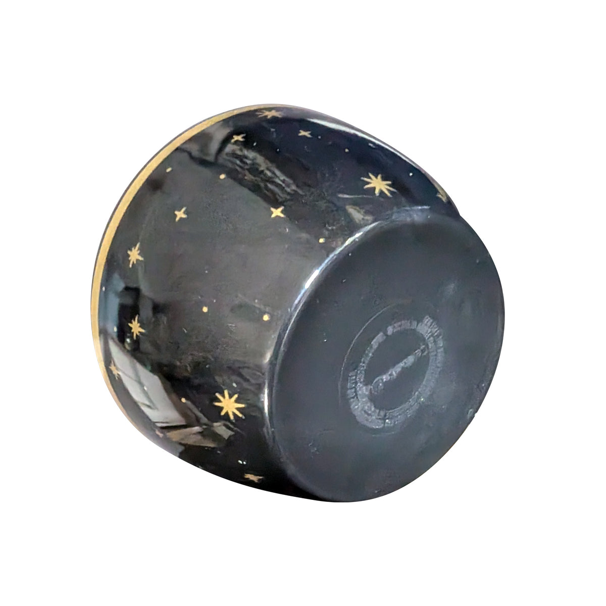 Black star candle tipped onto its rim on a white background, showing the gold stars painted across the underside of the bowl